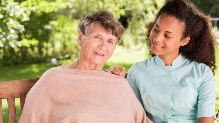 Idosa sentada no jardim com a cuidadora